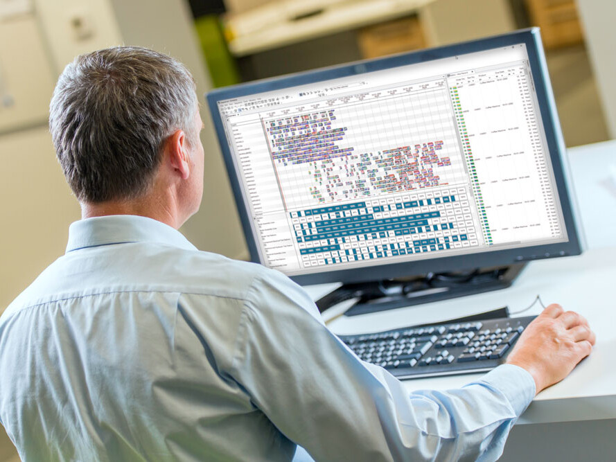 Mann von hinten sitzt an Schreibtisch und arbeitet an Computer mit Programmiercode auf Bildschirm