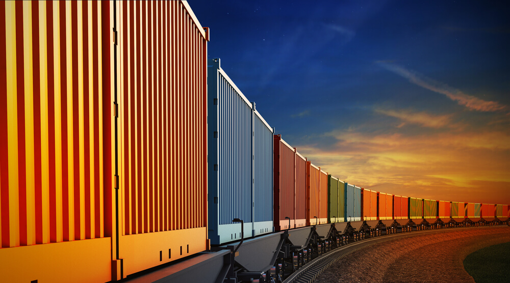 Lange Reihe bunter G&uuml;tercontainer auf Eisenbahnwaggons vor einem Abendhimmel