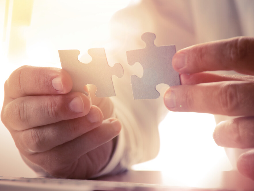 H&auml;nde halten zwei Puzzleteile, die zusammengef&uuml;gt werden sollen