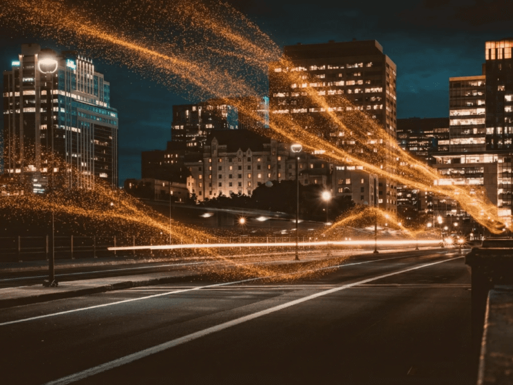 Nachtaufnahme einer Stadtstraße mit beleuchteten Hochhäusern und orangefarbenen Lichtspuren über der Straße